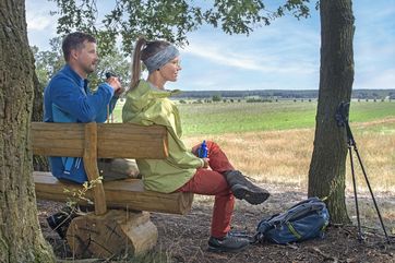 Zwei Wanderer genießen bei einer Rast auf den Kmehlener Bergen die weite Landschaft und den Ausblick in Richtung Sachsen
