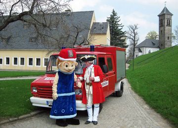 Maskottchen Löschi und Schließkapitän Clemens vor dem Löschfahrzeug der Festungsfeuerwehr